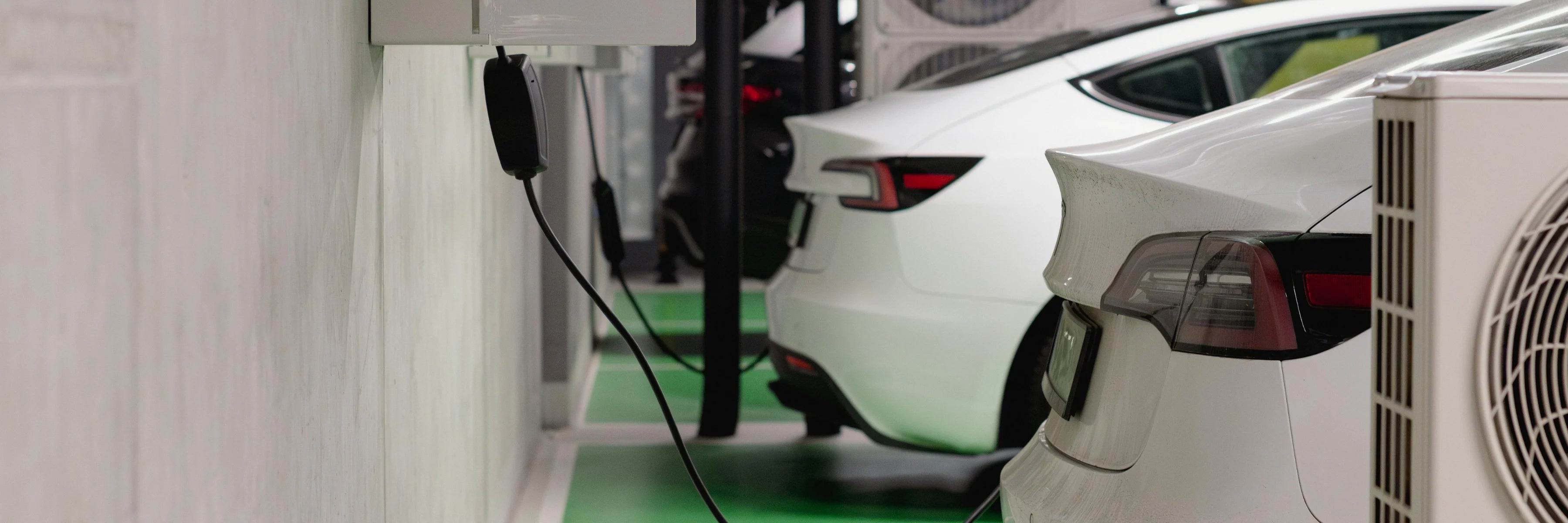 Electric car charging in covered business garage, wallbox unprotected, exposing cable and station to damage and wear