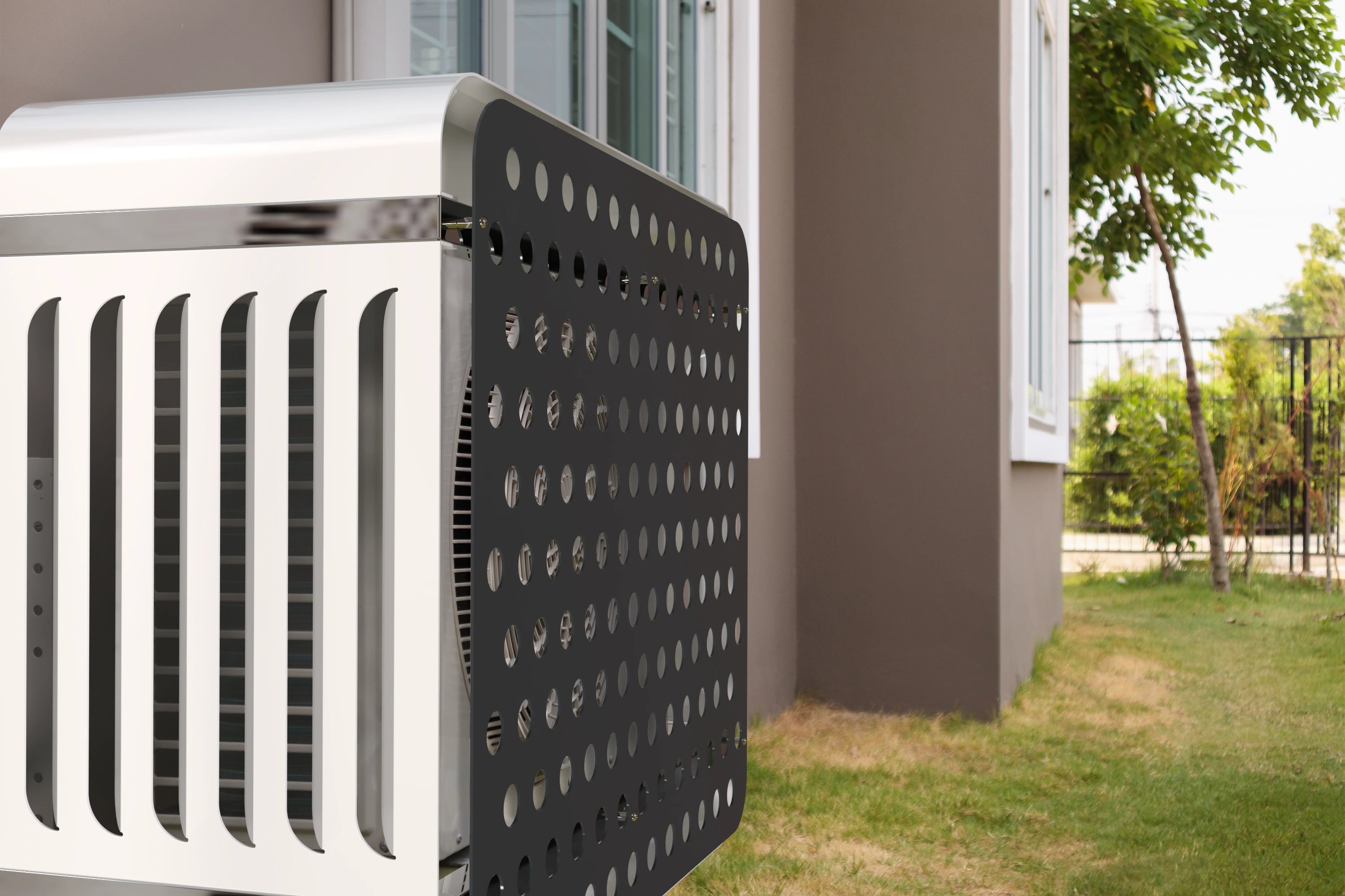 Zweifarbige Klimaanlagenabdeckung mit gelochter Front, an einem beigen Wohnhaus mit Garten montiert.