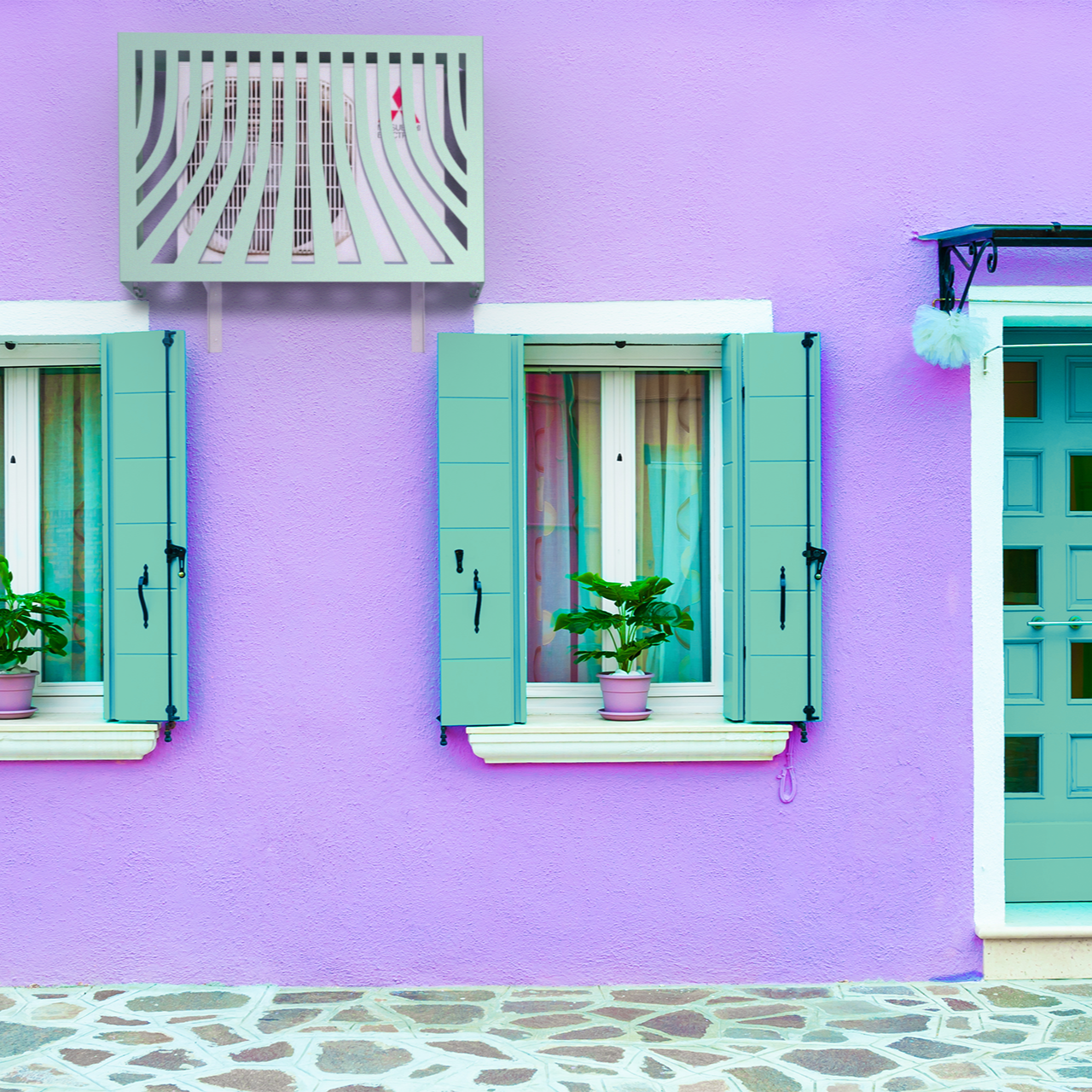 Cache clim romantique et protecteur – modèle Provence bleu installé contre mur de maison charmante lilas et azur. Protection sur Haier Tundra, compatible avec les unités de nouvelle génération en zones urbaines et résidentielles.