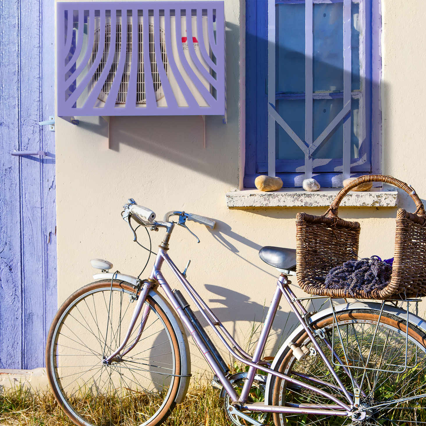 Dekorative und schützende Provence Abdeckung – lila an Hauswand installiert, passend zu architektonischen Details, Fahrrad darunter. Abdeckung auf Samsung Wind-Free – passend für energieeffiziente, moderne Außengeräte.