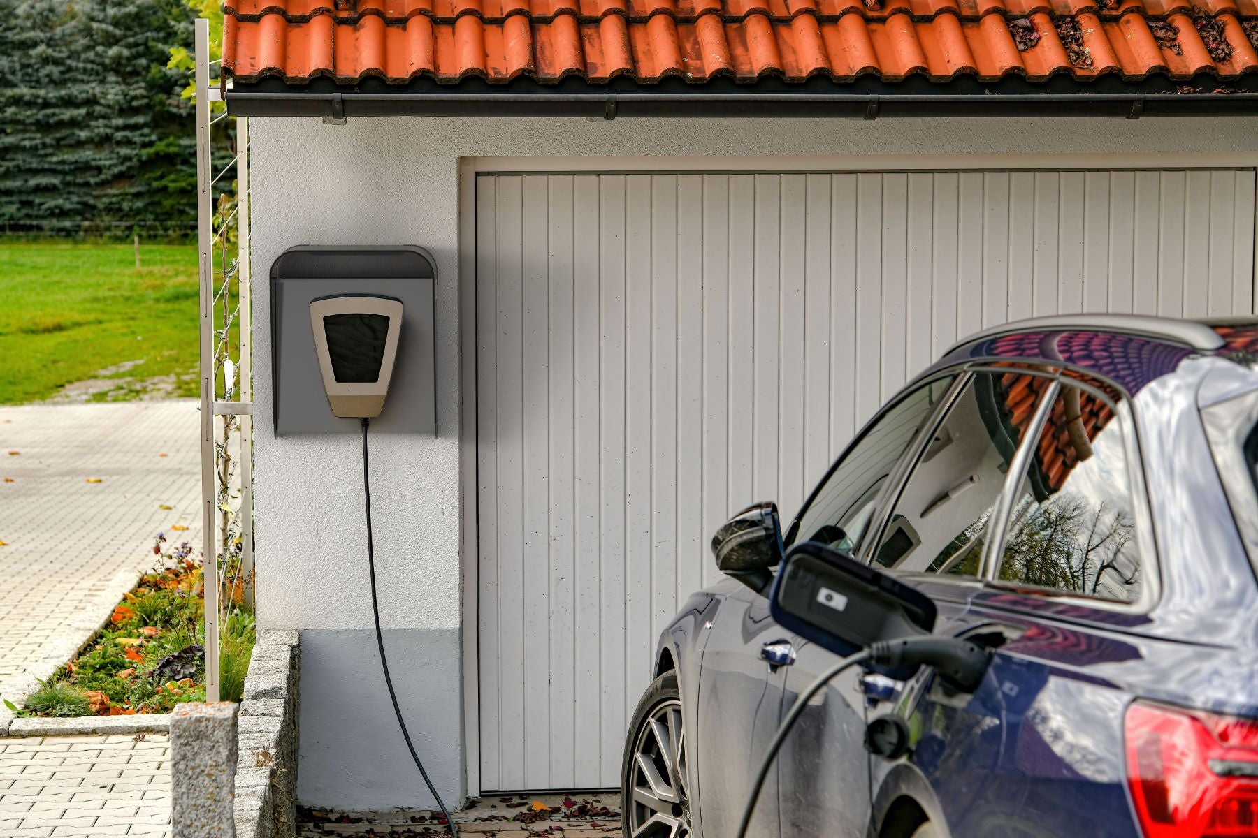 Garageansicht – Wallbox Cover Plus montiert an der Außenwand einer freistehenden Garage, Elektroauto im Ladevorgang, hochwertige technische Abdeckung für Kabel und Schutz. Kompatibel mit der Wandladestation Wallbox Commander 2.